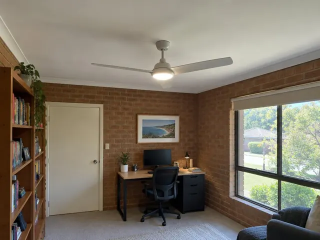 Ceiling fan in a brick-walled home office with a window and desk in Erina