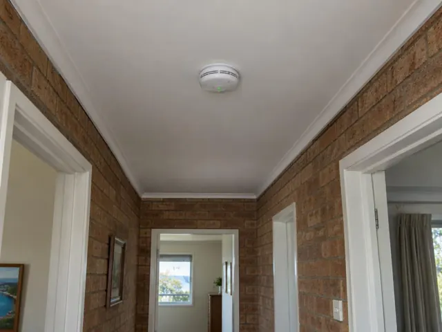 Ceiling smoke alarm in a brick hallway with white trim in Avoca Beach
